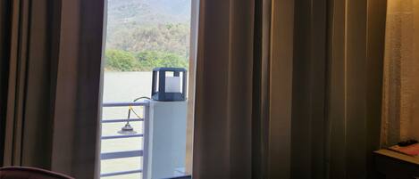 A hotel room with a bed, a chair, a window with curtains, and a view of a mountainous landscape.