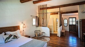 Een slaapkamer met een houten plafond, een bed met kussens, een stoel, een tafeltje en een lamp.