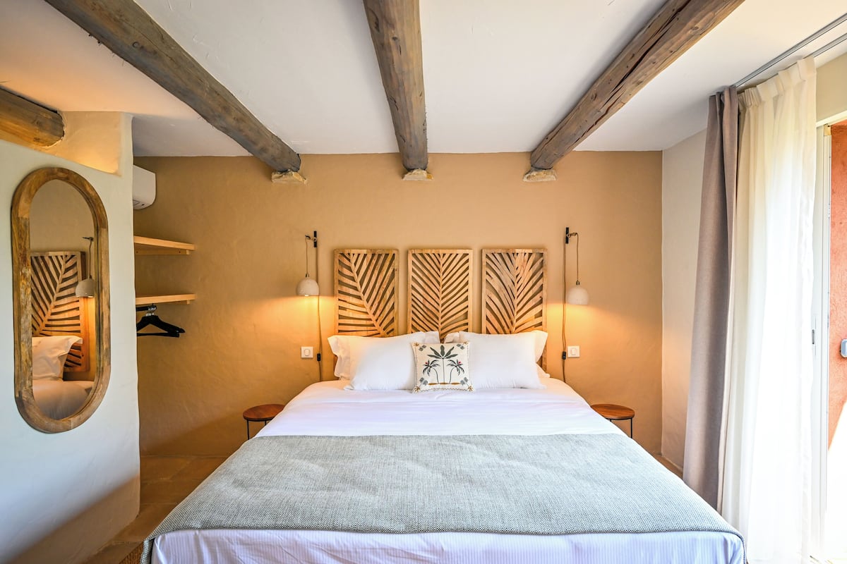 Ein Schlafzimmer mit einem großen Bett, einem hölzernen Kopfteil, zwei Nachttischen, einem Spiegel und einer Pendelleuchte.