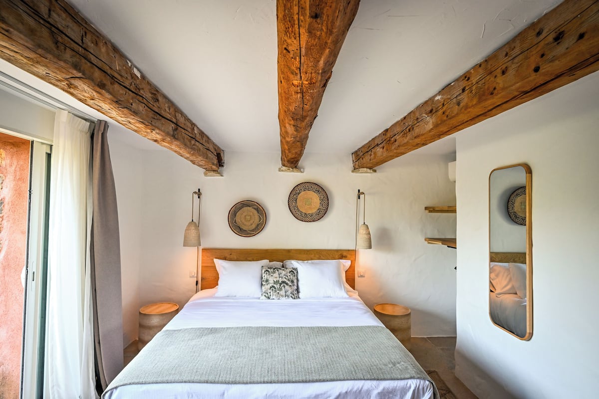 Ein Schlafzimmer mit einem großen Bett, Holzbalken an der Decke, zwei Nachttischen und einem Spiegel an der Wand.