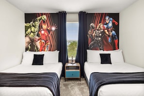 Quarto de hotel com duas camas, uma mesinha de cabeceira e um grande mural com tema de super-herói na parede.
