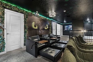 Um quarto com um sofá de couro preto, um sofá verde e uma parede com um mural.