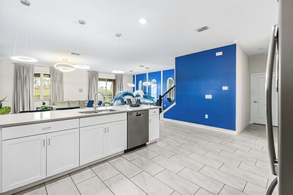 A modern kitchen with a large island, white cabinetry, and a blue accent wall.