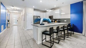 A modern kitchen with a central island, bar stools, and a blue accent wall. - Upstay Villa Sleeps 26 - Theater, Arcade, Pool (Kissimmee)