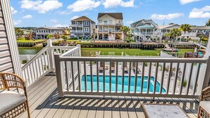 A wooden deck with a pool, overlooking a marina with boats and houses.