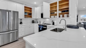 A modern kitchen with white cabinetry, stainless steel appliances, and built-in wooden shelves.