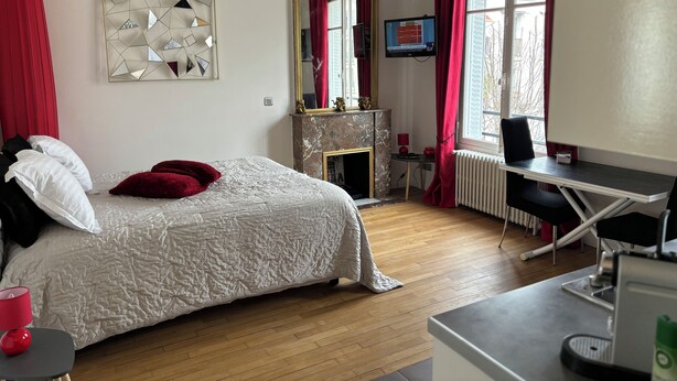 A bedroom with a bed, a desk, a fireplace, and a TV.