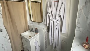 A bathroom with a marble wall, a sink, a mirror, a shower curtain, and a robe hanging on the door.