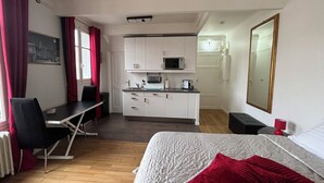 A compact hotel room with a bed, a desk, a kitchenette, and a bathroom.
