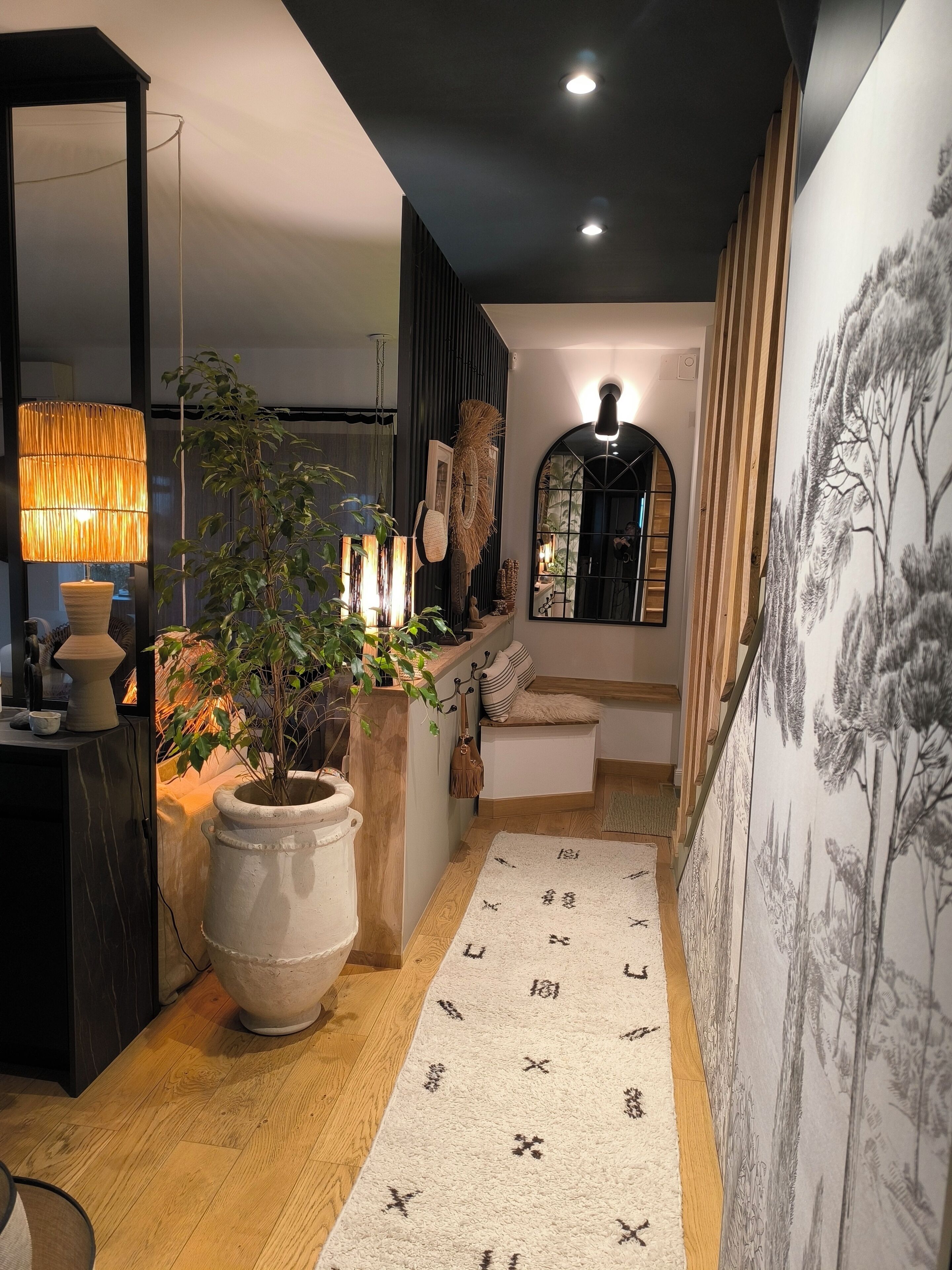 A hallway with a large potted plant, a lamp, a mirror, and a wall with a nature-themed mural.