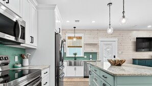 A modern kitchen with stainless steel appliances, teal cabinetry, and a wooden floor. - Coastal Retreat 3 Bedroom Home (Rockport)