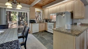 A kitchen with wooden cabinets, a granite countertop, a refrigerator, and a dining area with a table and chairs. - Sagebrush Cottage 3 Bedroom Chalet (South Lake Tahoe)