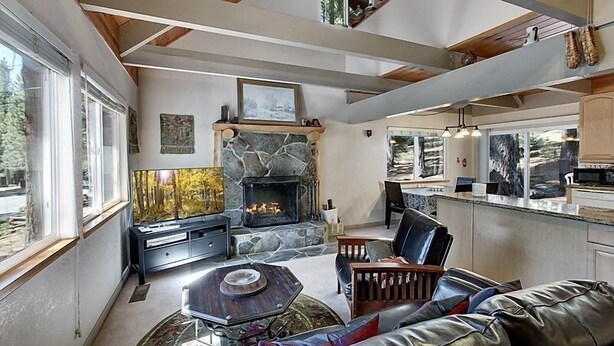 A modern living room with a stone fireplace, leather furniture, and large windows offering a view of the outdoors. - Sagebrush Cottage 3 Bedroom Chalet (South Lake Tahoe)