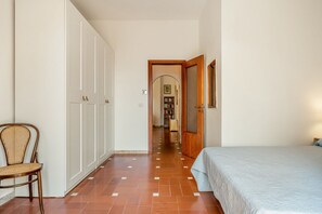 Een slaapkamer met een bed, een stoel, een kast en een gang naar een badkamer.