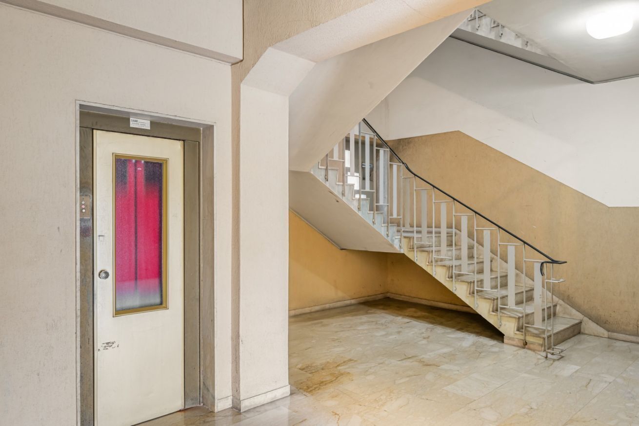 Interno di un hotel con pavimento in marmo, una scala con ringhiere bianche e una porta con tenda rossa.
