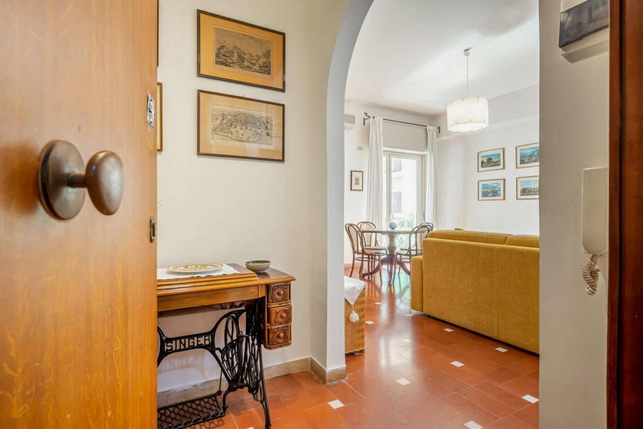 Une pièce comprenant un bureau en bois, une machine à coudre, une table à manger avec des chaises, un canapé et des tableaux encadrés accrochés au mur.