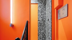 Un escalier avec des marches et une rampe noires, menant à une pièce dont le mur est texturé et où est accroché un tableau encadré.