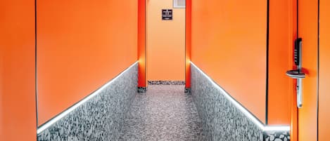 A corridor with a terrazzo floor and orange walls, leading to a door with a keypad lock.