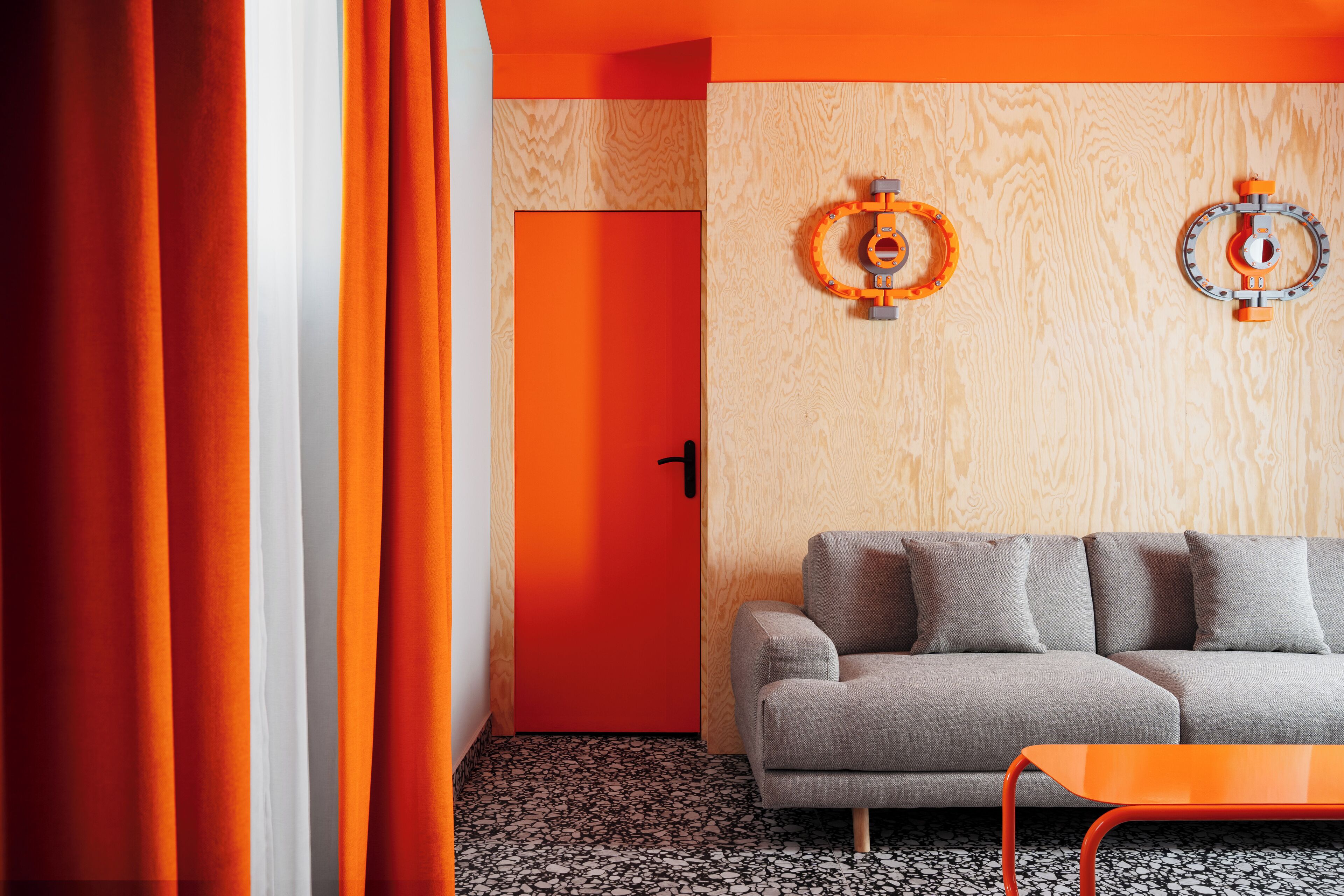 A modern living room with a grey sofa, orange curtains, and a wooden wall with two circular wall decorations.