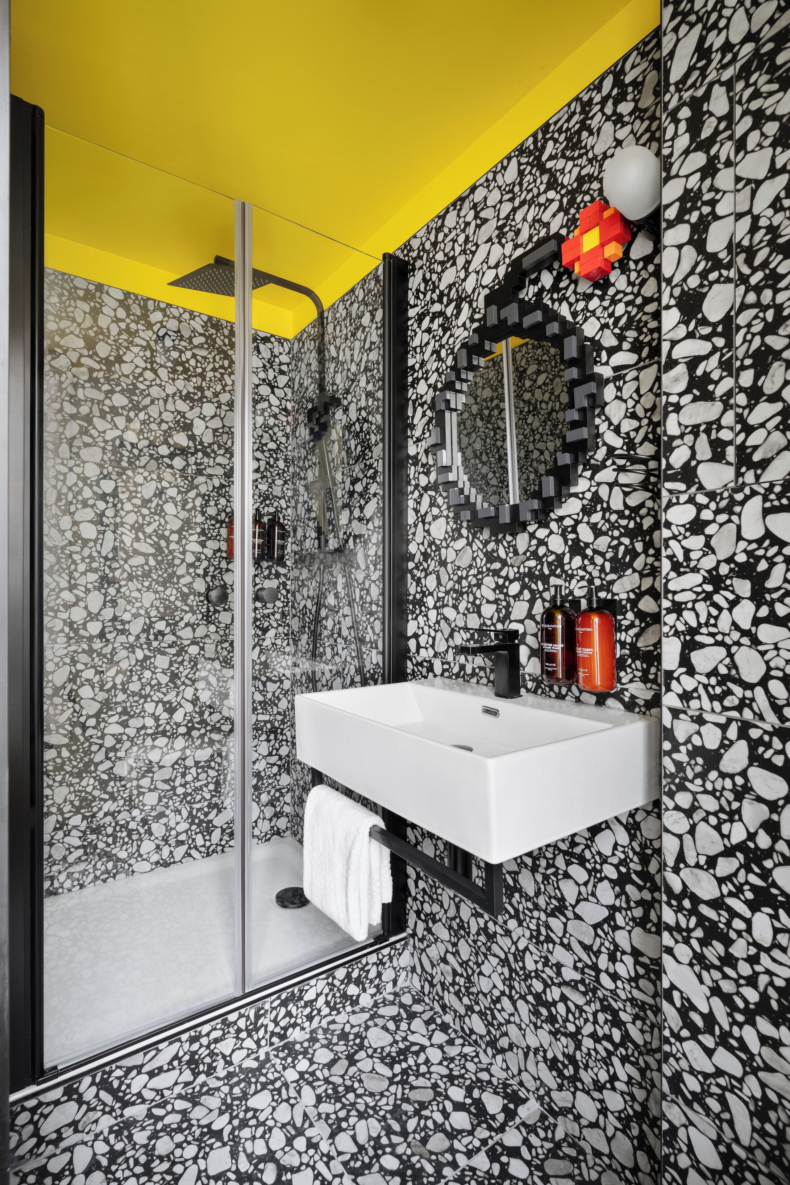 A modern bathroom with a white sink, a glass shower enclosure, and a mirror with a unique black and white mosaic backsplash.
