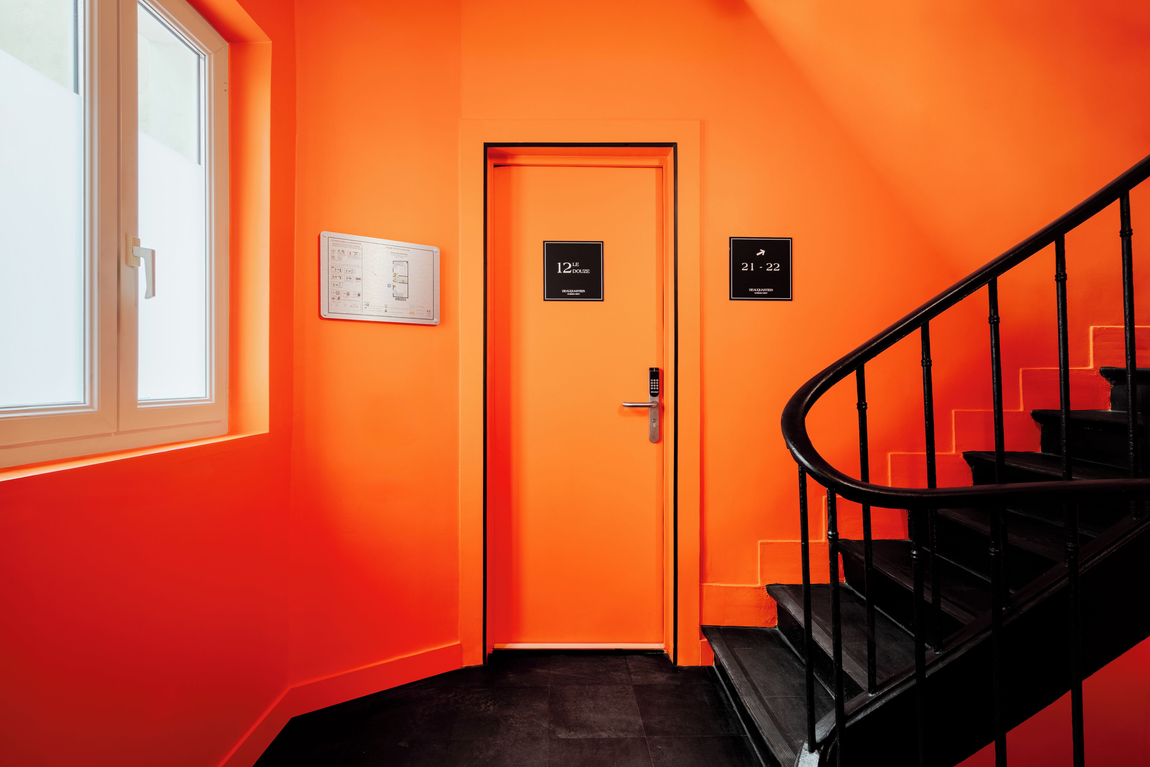 A hallway with a bright orange wall, a door labeled "12th HOUSE," and a staircase with black railings.