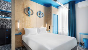 Une chambre d’hôtel moderne avec un grand lit, des murs recouverts de panneaux en bois, un mur d’accent bleu et une salle de bain avec un rideau de douche bleu.
