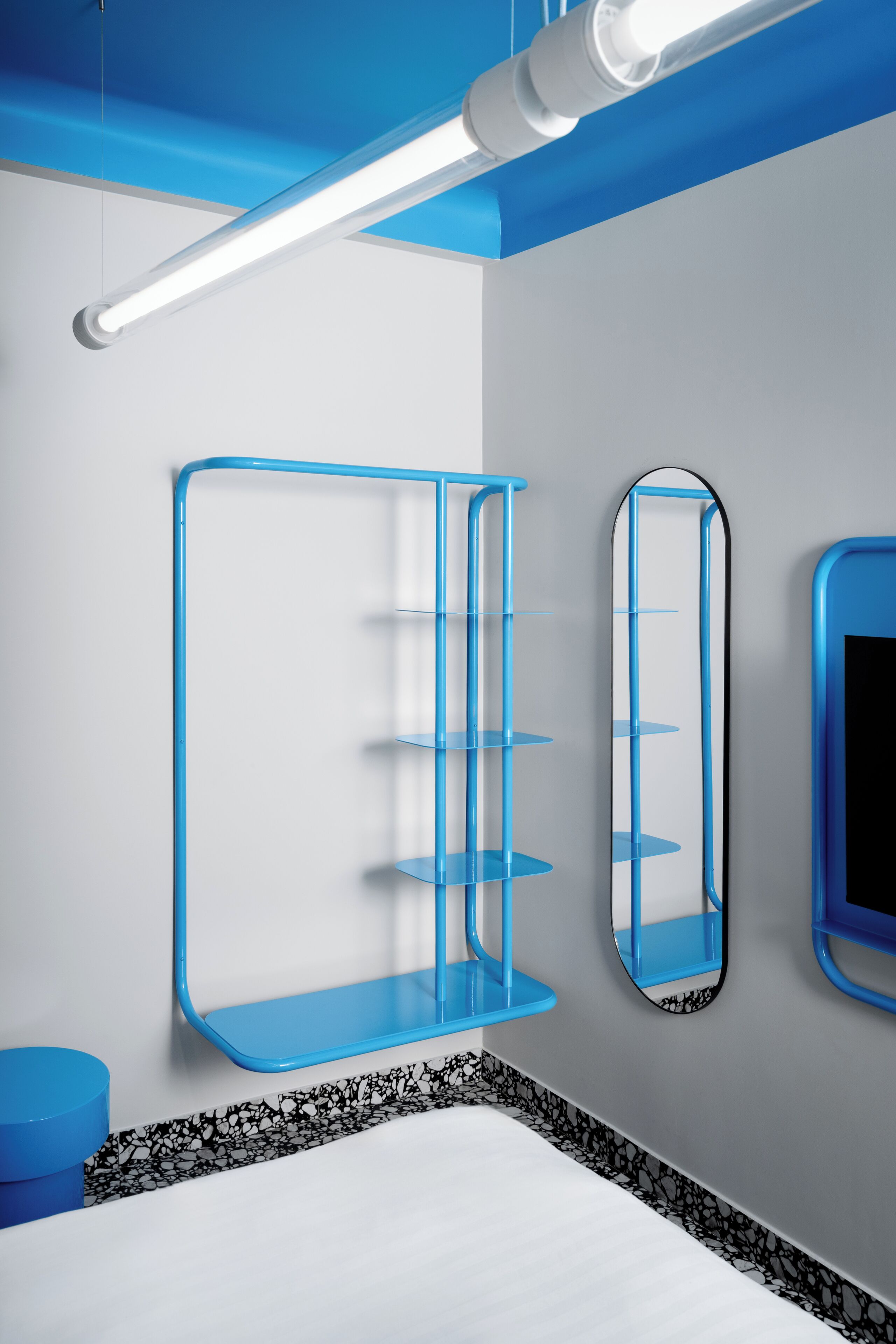 A modern bedroom with a bed, a blue shelving unit, a mirror, and a blue accent wall.