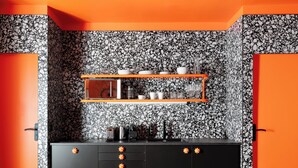 Une cuisine moderne avec un crédence noire et blanche à motifs, des meubles de rangement orange et un îlot central doté de tabourets.