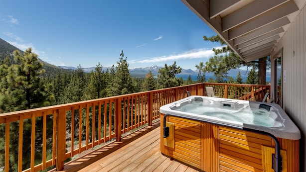 Una terraza de madera con un jacuzzi y vistas a montañas y un lago.