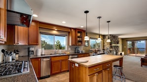 Una cocina amplia con armarios de madera, encimeras de granito y una isla grande. Hay luces colgantes y una pared decorativa de piedra.