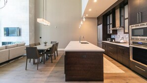 Une cuisine moderne dotée d’un grand îlot central, de meubles de couleur sombre, d’appareils électroménagers en acier inoxydable et d’un coin repas avec un canapé et des fauteuils.