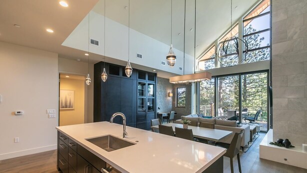 Une cuisine moderne dotée d’un îlot central, de luminaires suspendus et d’un coin repas offrant une vue sur l’extérieur.