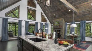 A spacious kitchen with a large island, wooden beams, and large windows offering views of the outdoors. - Oakhaven Fell - Couples Retreat - Sauna - Cold Plunge - Hot Tub (Broken Bow)