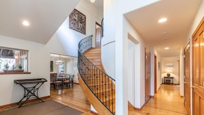 Un interior espacioso con una escalera de madera, un comedor y un pasillo que lleva a una puerta.