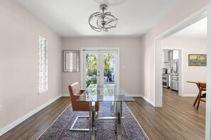 A modern dining area with a glass table, brown leather chairs, a patterned rug, and a view of the kitchen.