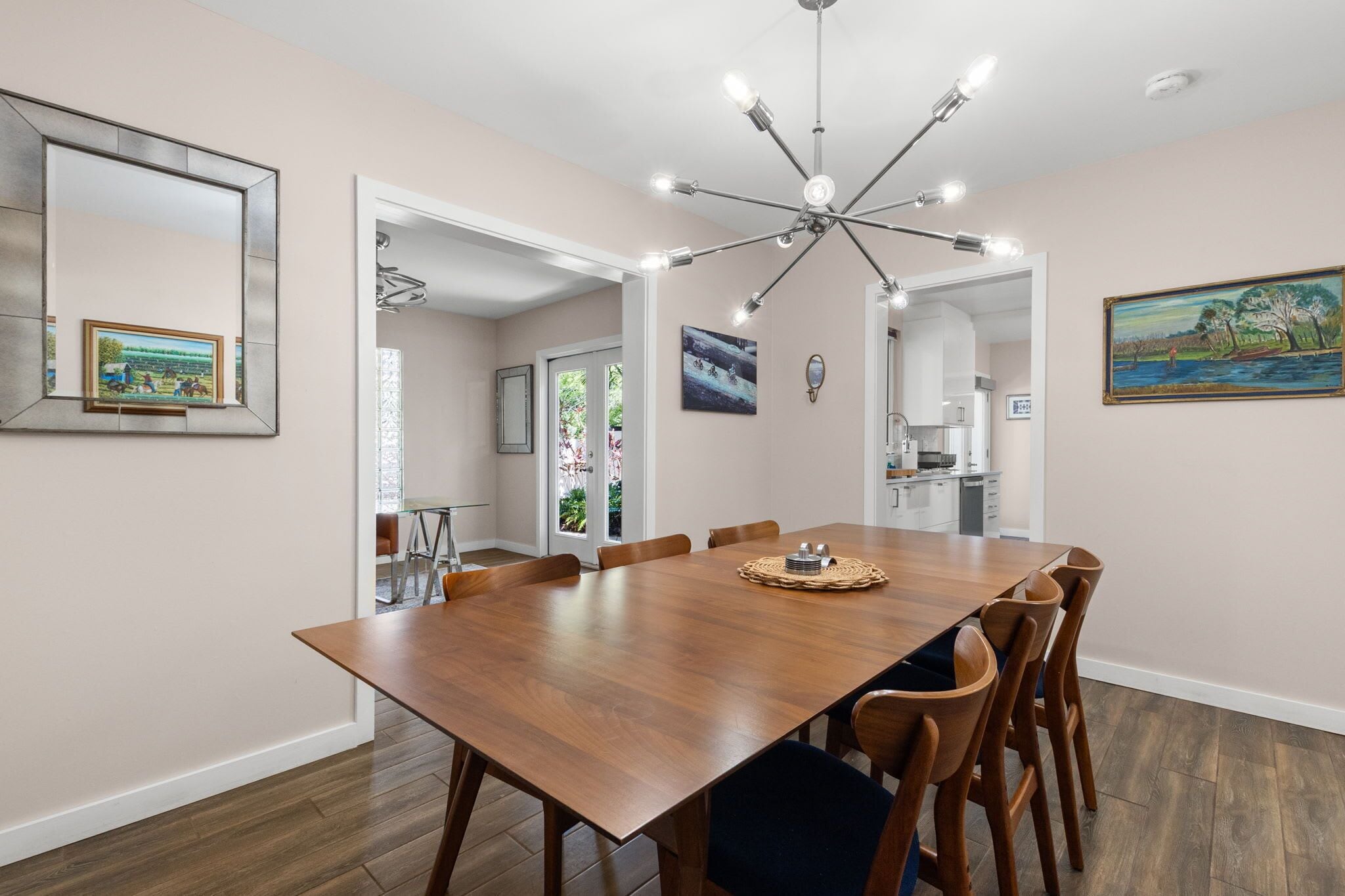 A dining room with a wooden table, chairs, a chandelier, and artwork on the walls.