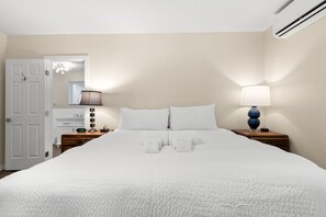 A neatly made bed with white linens, a bedside lamp, and a clock on the nightstand. - NEW! Sunset Serenity | South Tampa Home with Pool (Tampa)