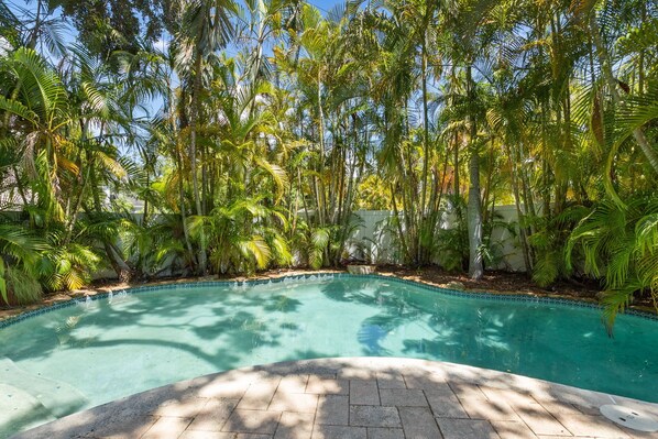 A swimming pool surrounded by tall palm trees and a stone pathway leading to the pool.