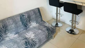 Ένα δωμάτιο με έναν καναπέ, δύο σκαμπό μπαρ, έναν πίνακα, έναν καθρέφτη και έναν λευκό πάγκο.