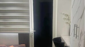 Ένα δωμάτιο με ένα κρεβάτι, μια καρέκλα, μια πόρτα και έναν τοίχο με υφή που μοιάζει με μάρμαρο.
