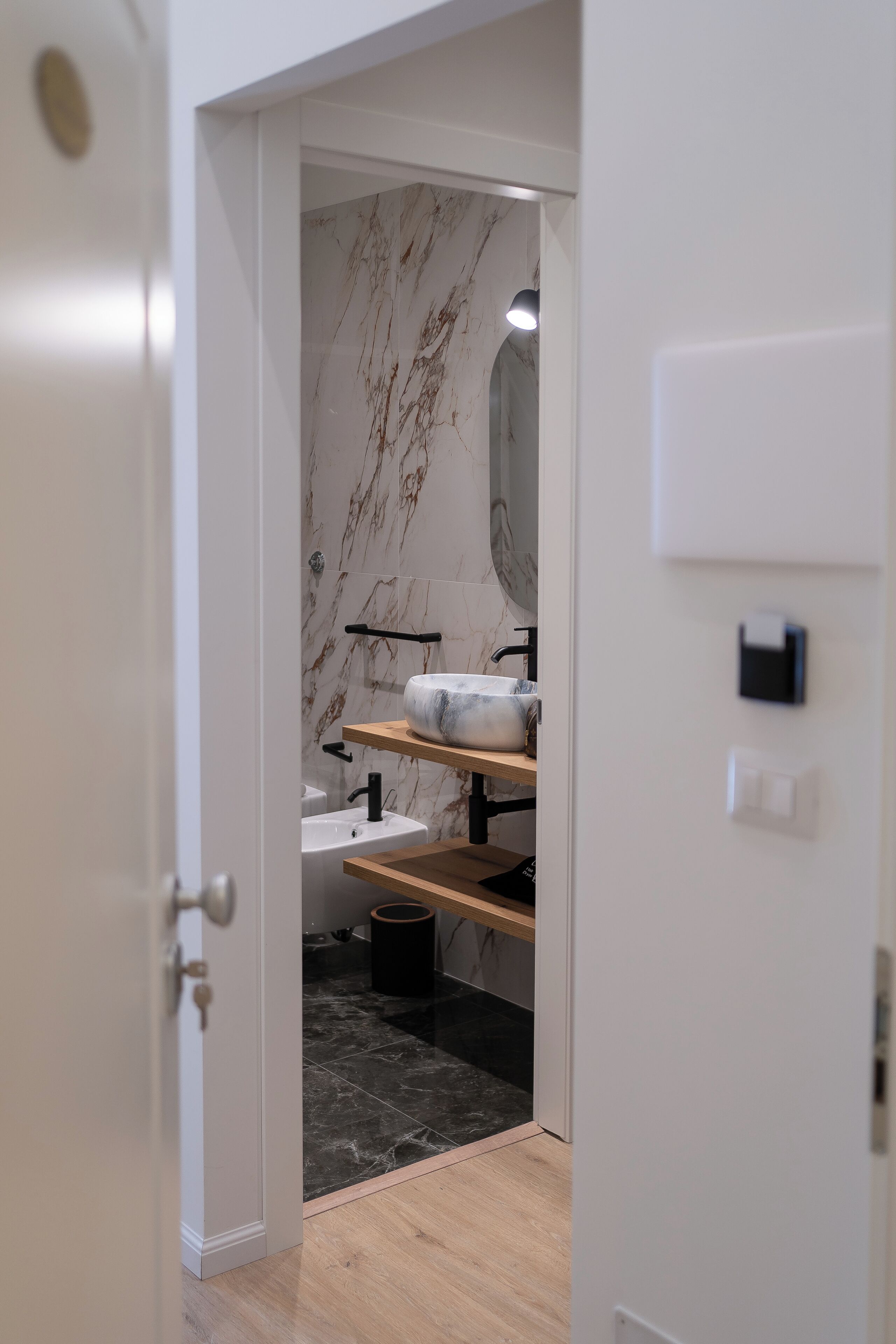 Ein modernes Badezimmer mit Marmorfliesenspiegel, einem Waschbecken mit Spiegel darüber und einem hölzernen Ablagebrett.