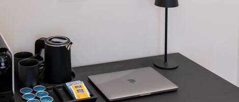 Une chambre d’hôtel avec un miroir rond, un lit avec une literie blanche, une table de chevet noire avec une lampe, un ordinateur portable et un coin café.