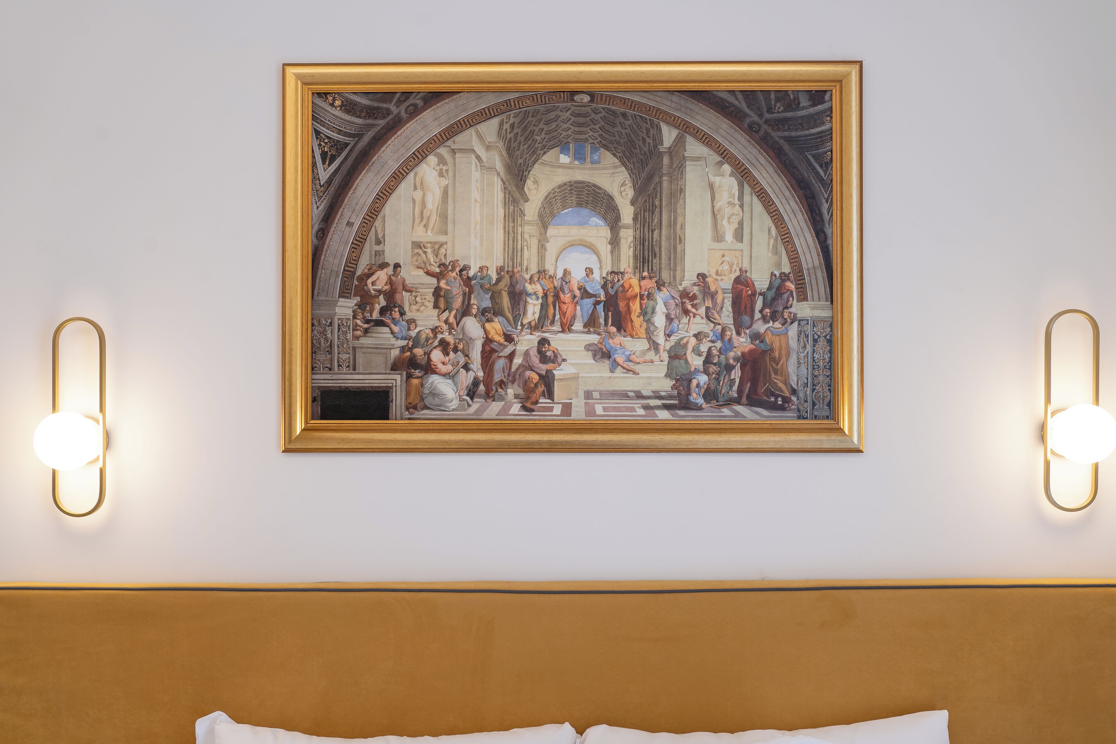 Hotellihuone, jonka seinällä on suuri, klassinen maalaus, ja jossa on valkoisilla lakanoiden peitetty sänky sekä kaksi seinävalaisinta.