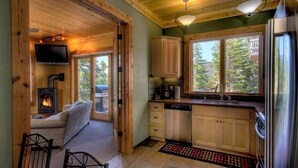 Ein gemütliches Blockhaus mit Kamin, Holzmöbeln, einer Küche mit Holzausstattung und einem großen Fenster mit Blick auf Bäume.