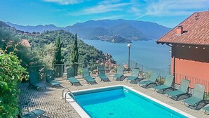 A pool area with lounge chairs, a clear view of a lake, and mountains in the background.