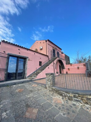 Un edificio rosa con una escalera que conduce a una entrada, adoquinado de piedra y una verja metálica.