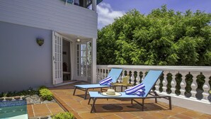 Zona junto a la piscina con dos sillas de descanso, una mesita y un muro decorativo.