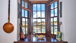 Habitación de esquina con ventanas amplias, una guitarra, un cuenco y un cuadro en el alféizar.