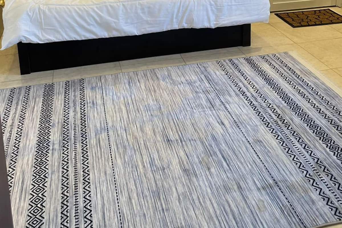 A neatly made bed with white linens, a patterned rug, and a wall-mounted air conditioner.
