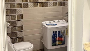 A bathroom with a toilet, a shower, and a washing machine. -  Nozzle Al Matal Serviced apartments  (Abha)
